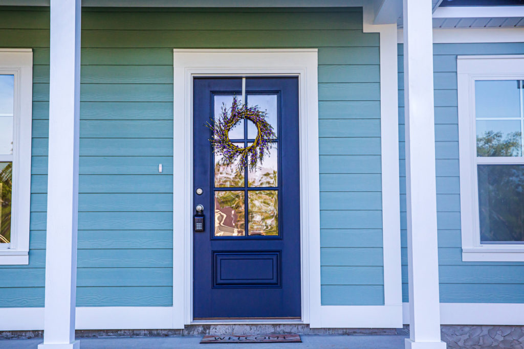 Blue front door of a brand new construction house with blue siding, a  ranch style home with a yard